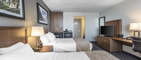 A hotel room with two beds, a desk, a TV, and a bathroom visible through an open door.