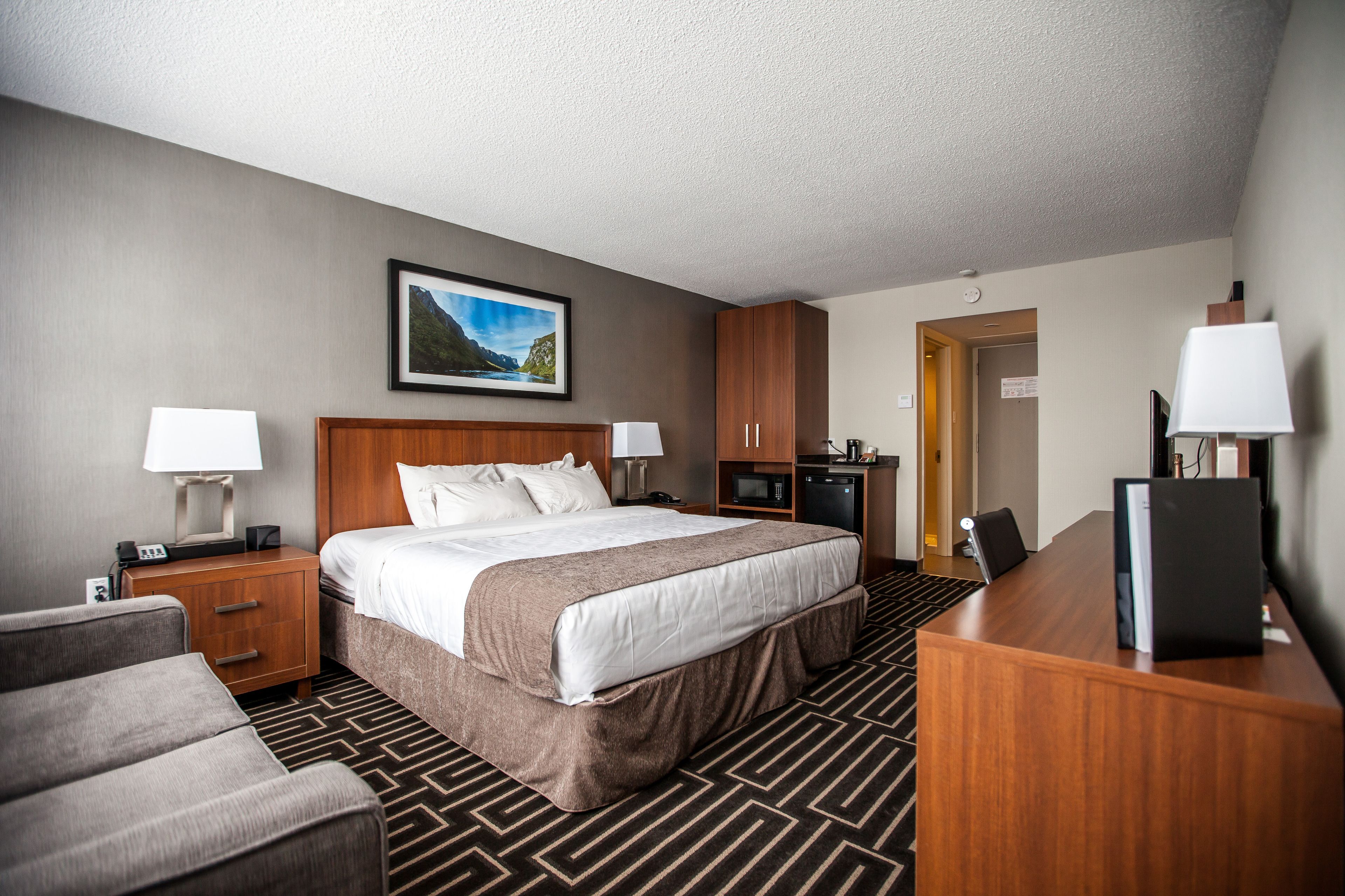 A hotel room with a large bed, two bedside tables with lamps, a desk with a chair, a microwave, and a television.