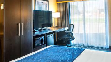 Una habitación de hotel con una cama, un escritorio con televisión, un microondas y una silla.