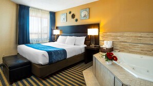 A hotel room with a large bed, a nightstand with lamps, a bathroom with a bathtub, and a window with curtains.