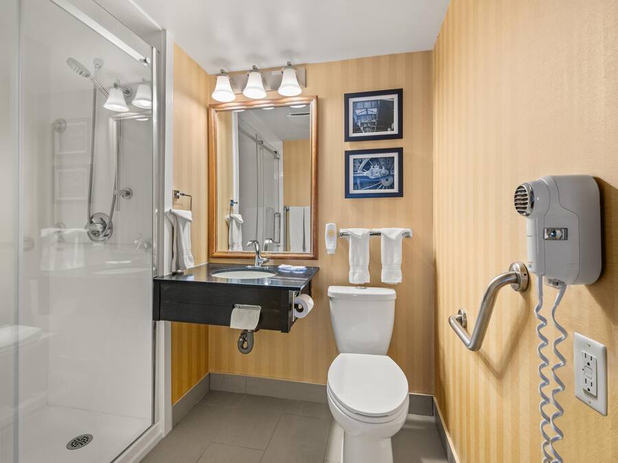 A modern bathroom with a glass shower enclosure, a sink with a towel rack, a toilet, and a hairdryer mounted on the wall.