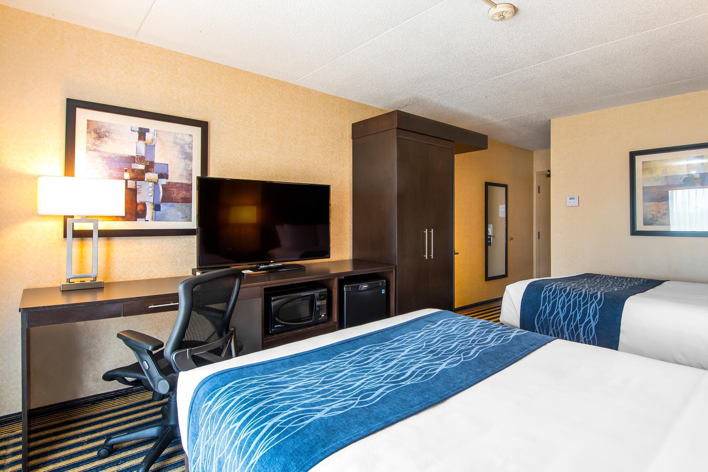 A hotel room with a bed, a desk with a TV, a microwave, and a chair.
