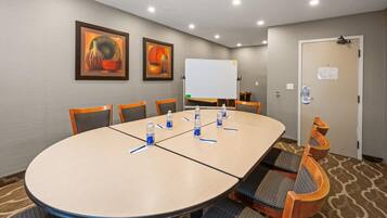 Un salón de conferencias con una gran mesa ovalada, seis sillas, una pizarra y dos cuadros en la pared.