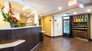 A reception area with a reception desk, a plant, a refrigerator stocked with beverages, and snack shelves.