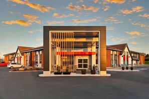 A modern building with a central entrance, large windows, and outdoor seating areas.