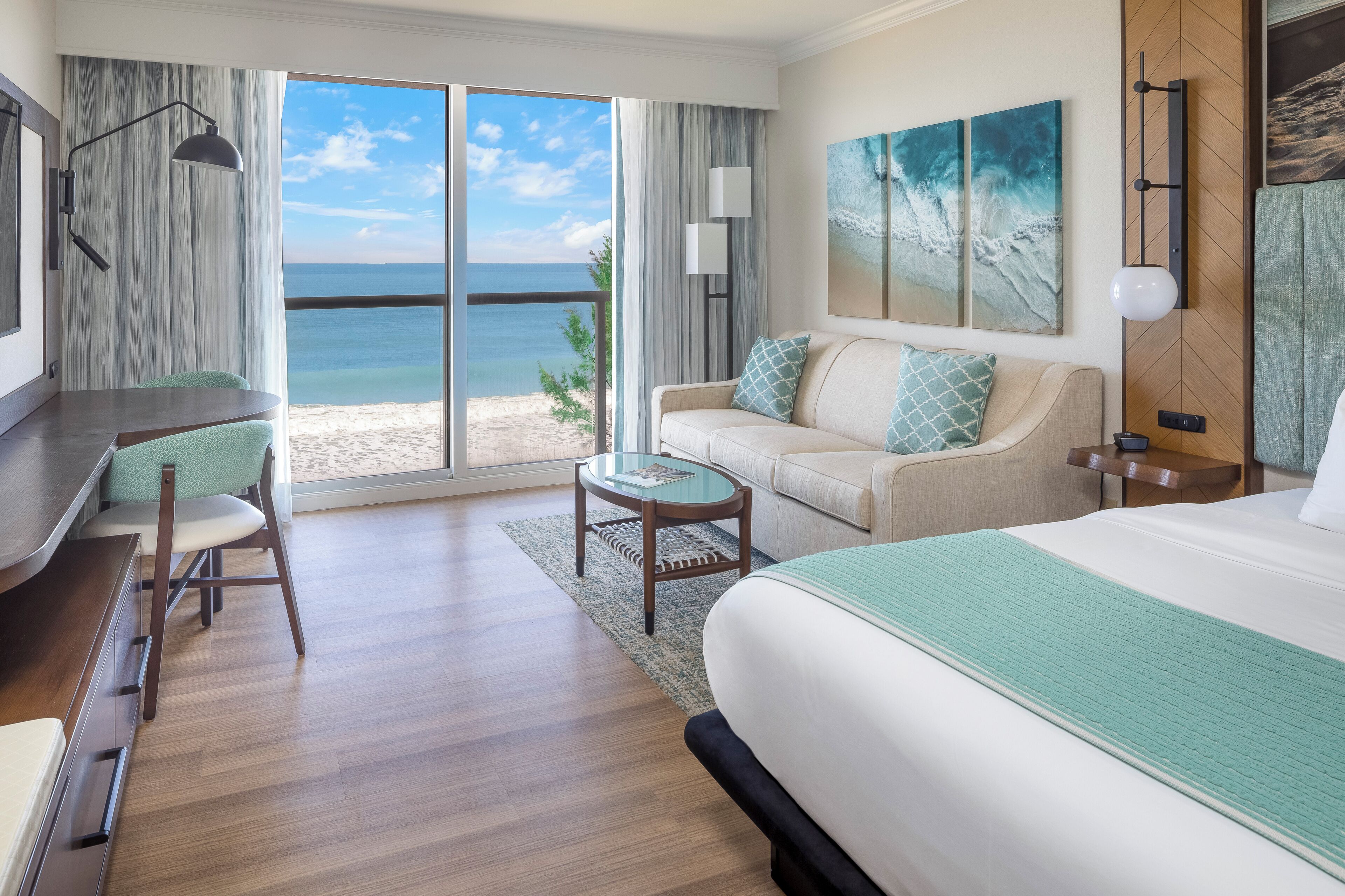 A hotel room with a large bed, a sofa, a desk, and a view of the beach.