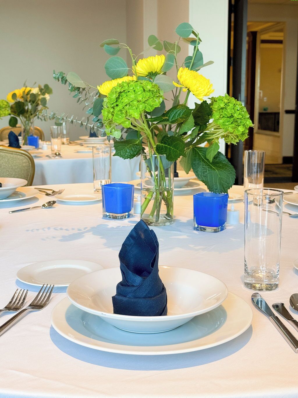A dining table set with plates, cutlery, and a centerpiece of yellow flowers.