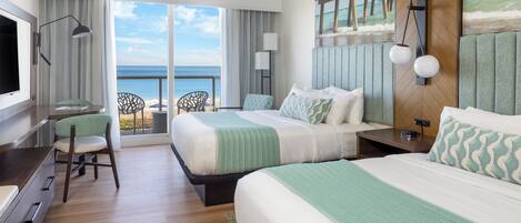 A hotel room with two beds, a desk, a chair, and a view of the ocean.