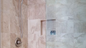 A shower with a handheld showerhead and a glass door.