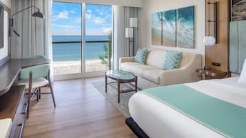 A hotel room with a large bed, a sofa, a desk, and a view of the beach.