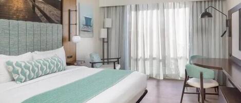 Una habitación de hotel con una cama grande, un escritorio, una silla, una lámpara y un cuadro en la pared.