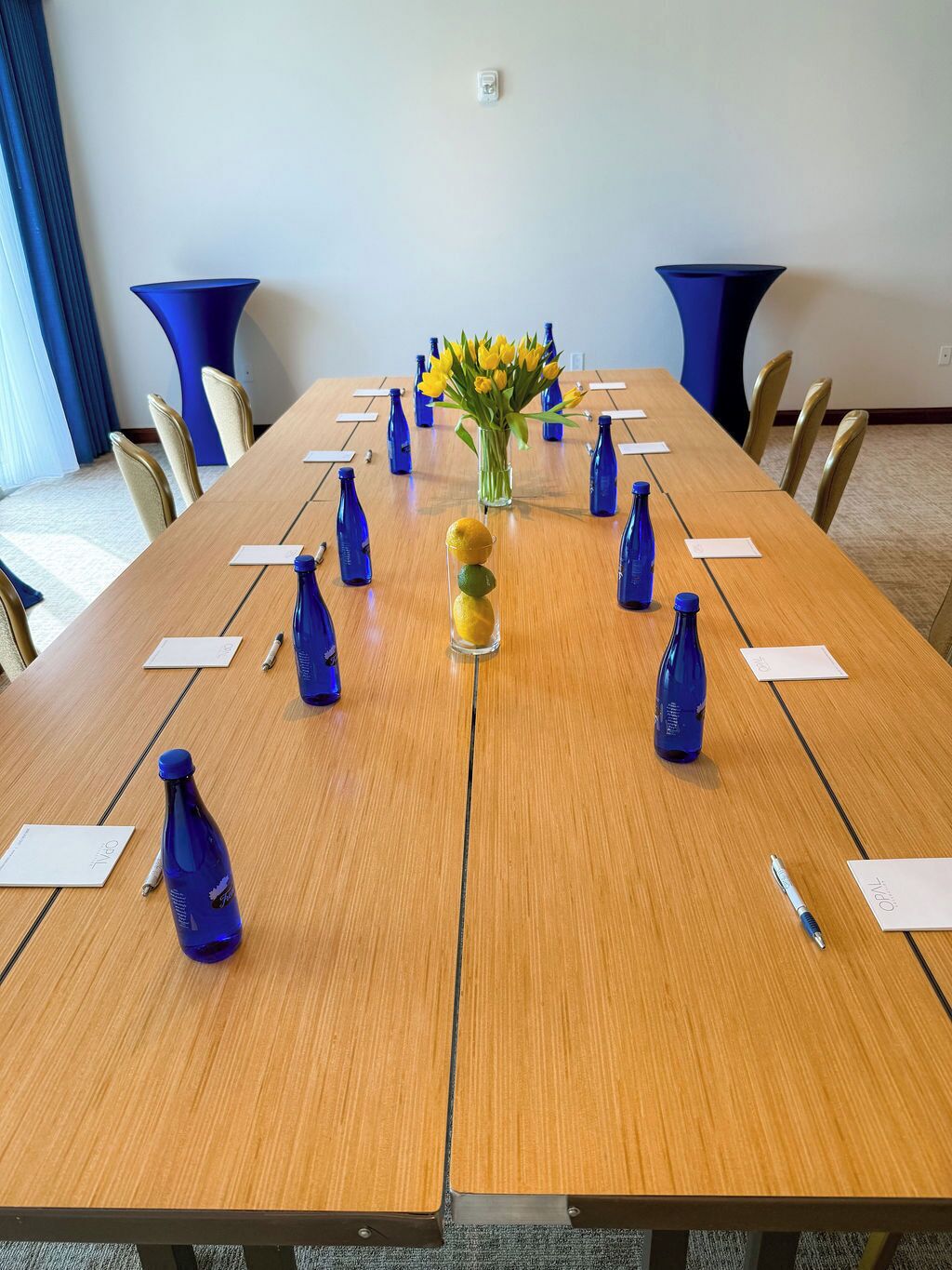 A conference room with a long wooden table, blue chairs, and a vase with yellow flowers.