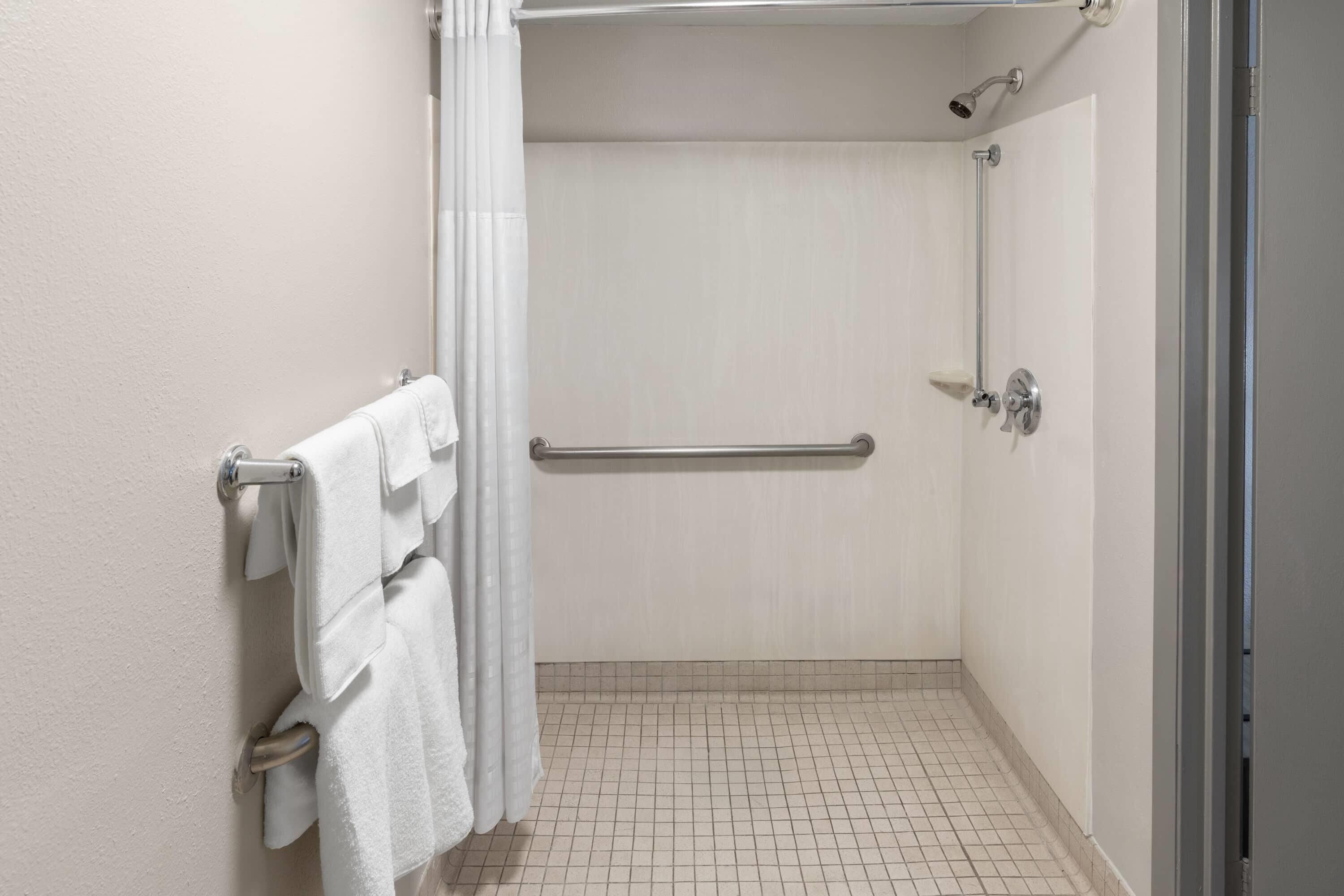 Un baño pequeño y limpio con ducha, toallero y barra de apoyo.