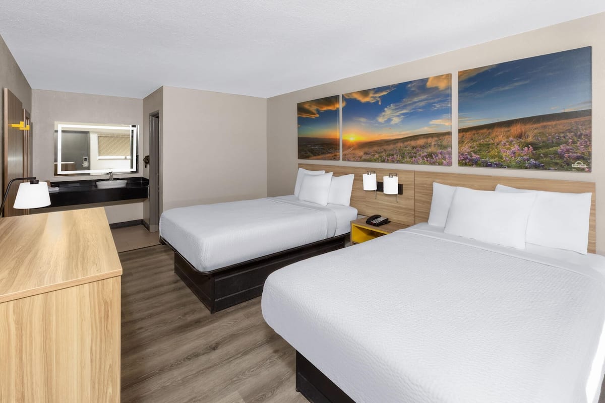 Habitación de hotel con dos camas, un escritorio, un espejo y obras de arte en la pared.