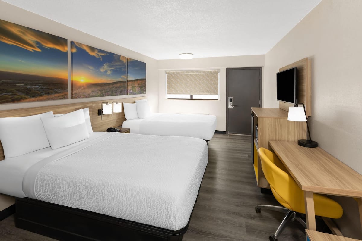 A hotel room with two beds, a desk, a chair, a TV, and a window with blinds.