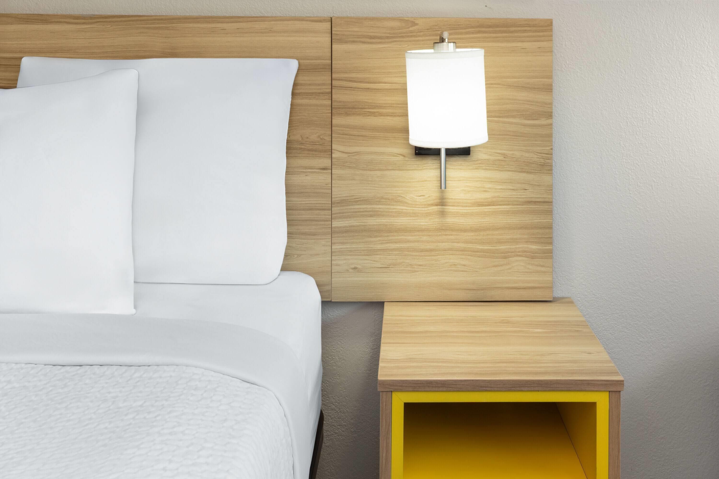 A neatly made bed with white linens, a wooden headboard, and a bedside table with a lamp.