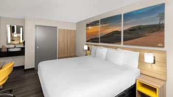 Une chambre d’hôtel avec un grand lit, un bureau avec une chaise, un miroir et deux lampes fixées au mur.