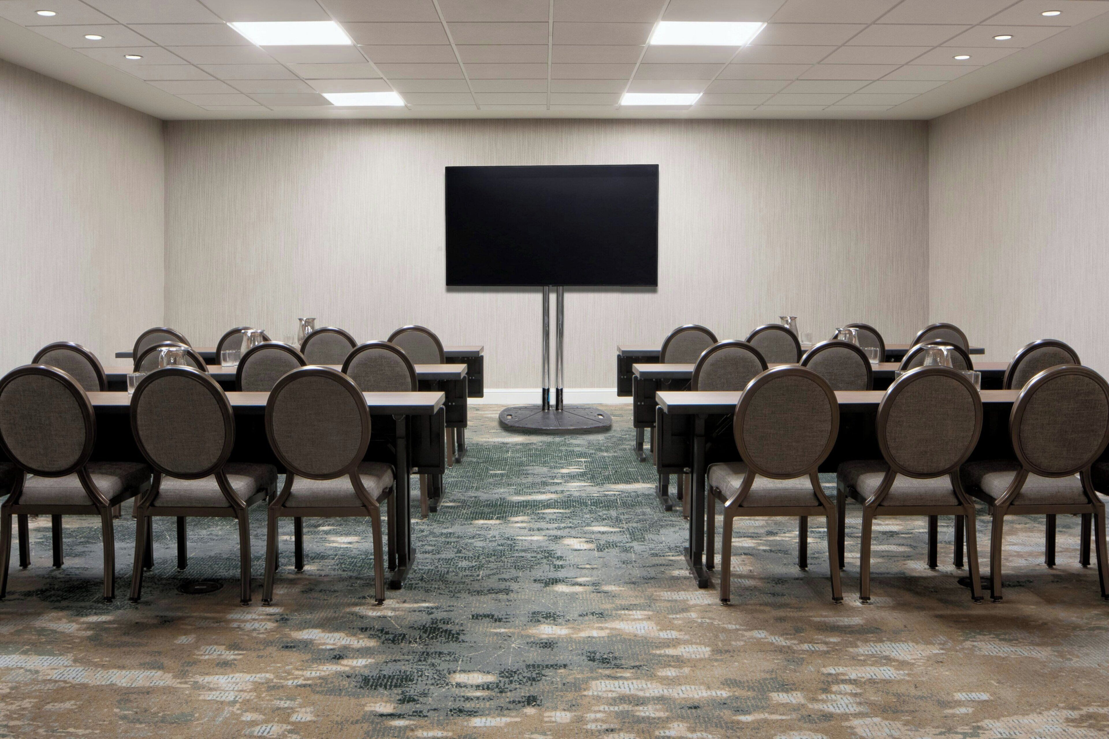 A conference room with a large flat-screen TV, multiple tables with chairs, and a patterned carpet.