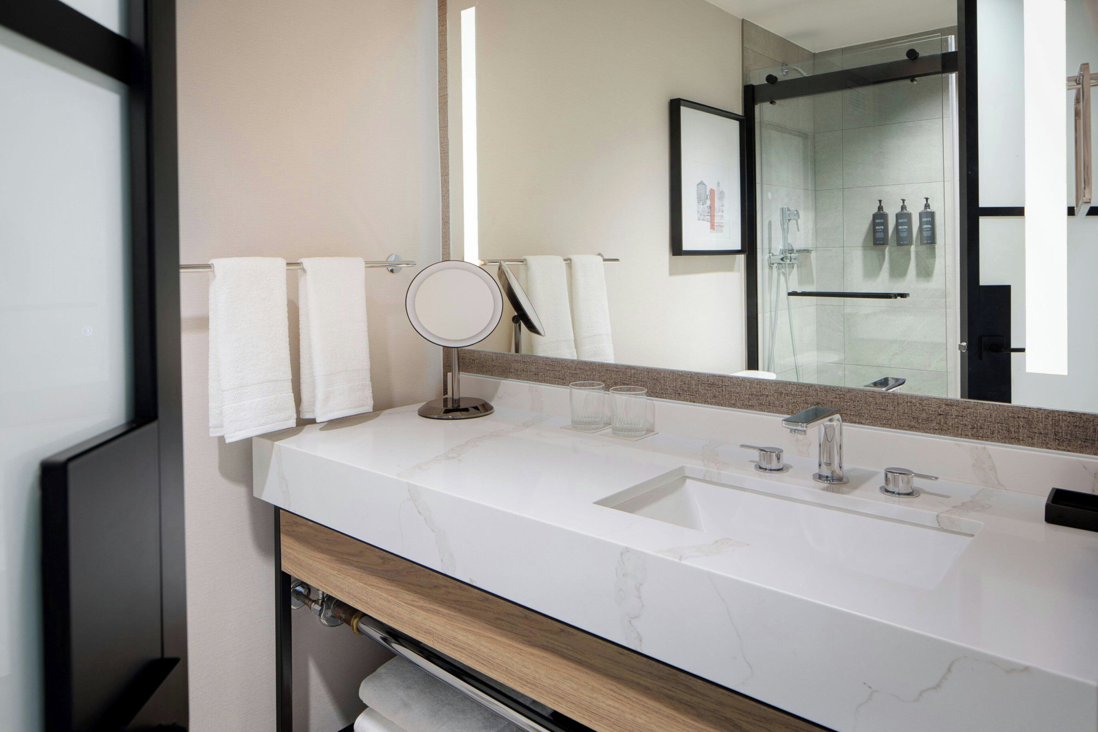 Een moderne badkamer met een wastafel van wit marmer, een ronde spiegel en een douchecabine met glazen wanden.
