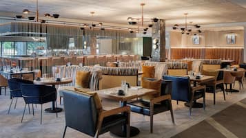 A modern restaurant with multiple seating areas, including booths and tables, and a bar in the background.
