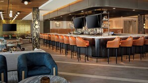 Un área de bar moderna con una barra curva, varios taburetes y un televisor montado en la pared.