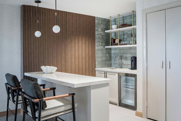 Cocina moderna con una isla central, dos lámparas colgantes, un salpicadero de ladrillo integrado y un refrigerador blanco.