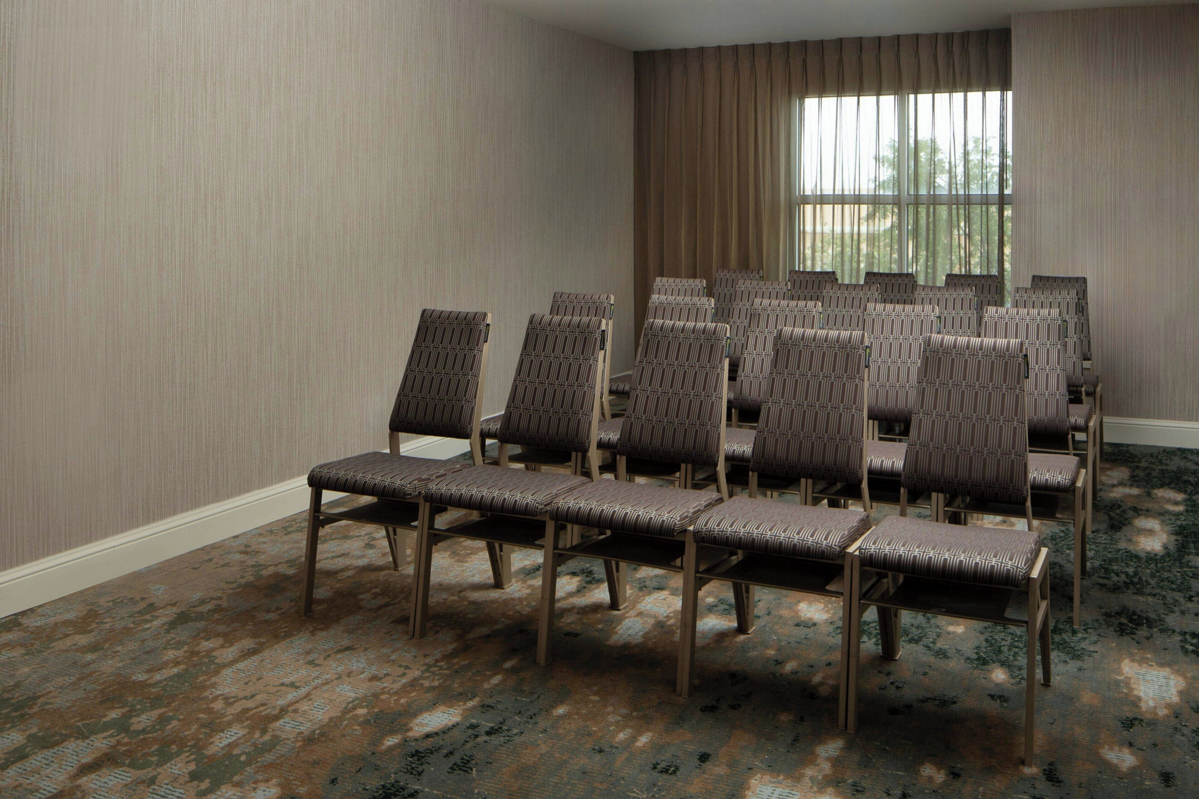 A conference room with rows of chairs, a large window, and a patterned carpet.