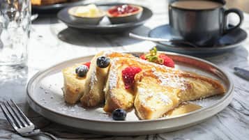 A breakfast plate with French toast, blueberries, and strawberries, accompanied by a cup of coffee and a glass of water.