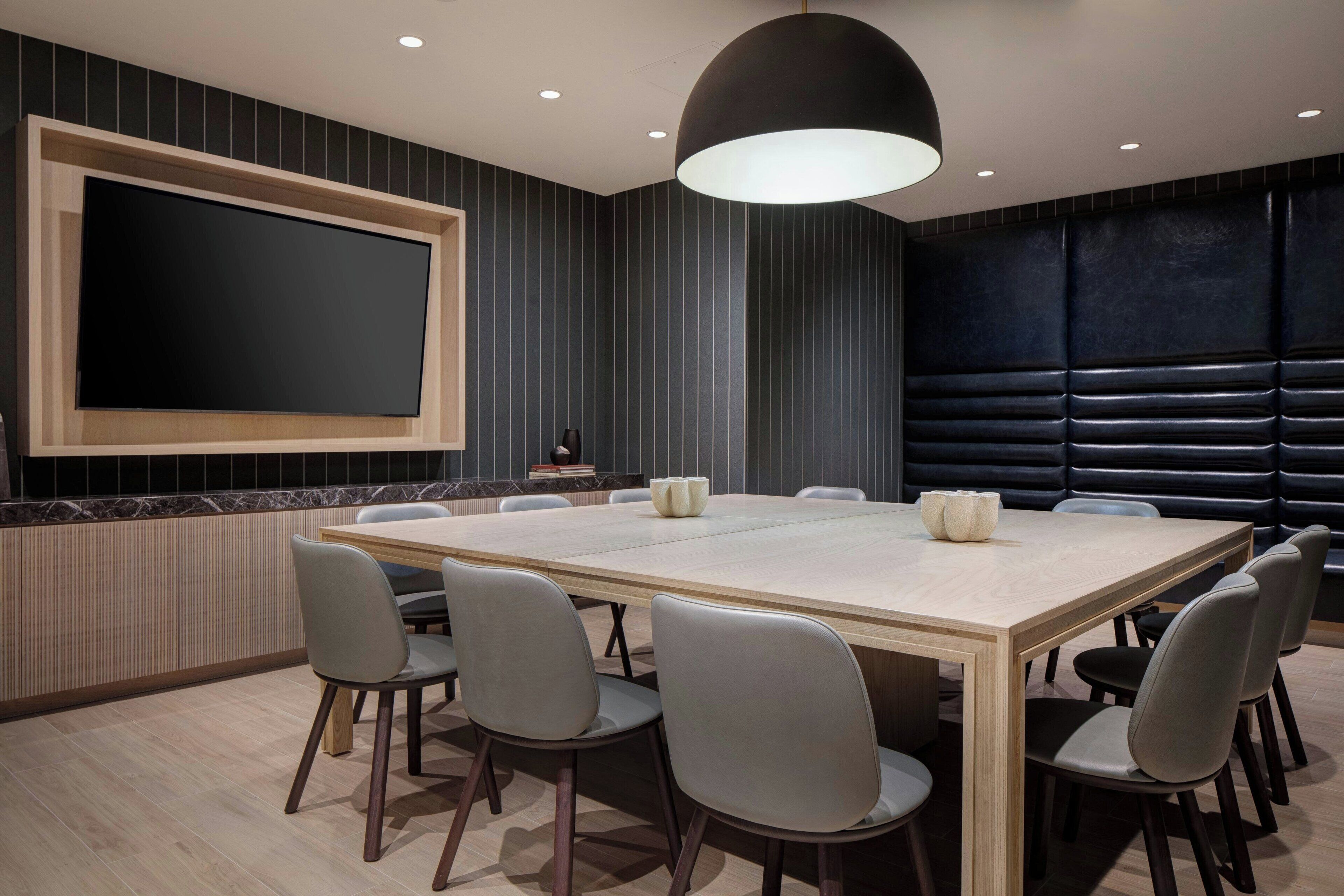 A conference room with a large table, chairs, a flat-screen TV, and a modern light fixture.