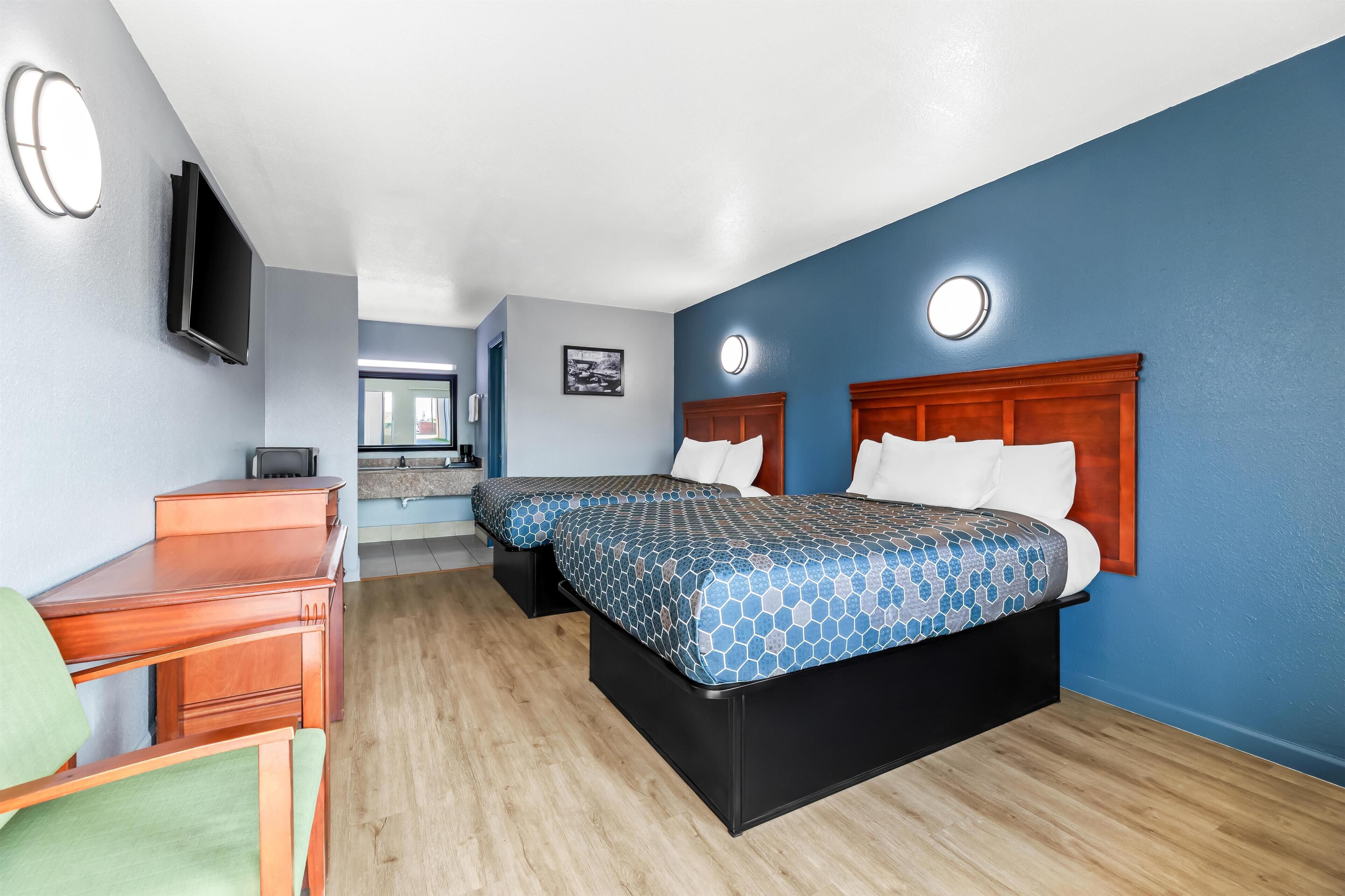 A hotel room with two beds, a desk, a chair, and a TV mounted on the wall.