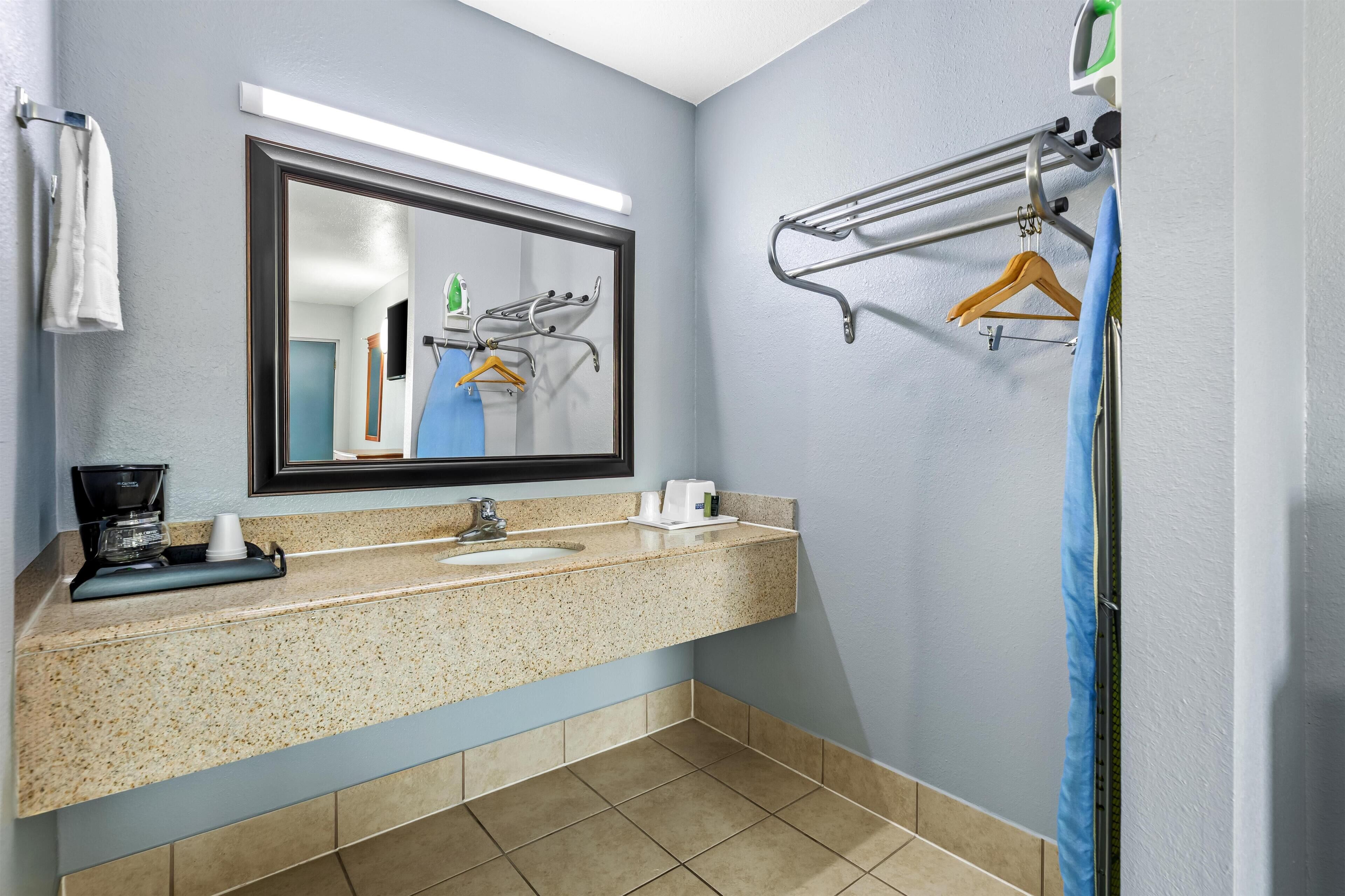 A bathroom with a granite countertop, a sink, a mirror, a towel rack, and a shower curtain rod.