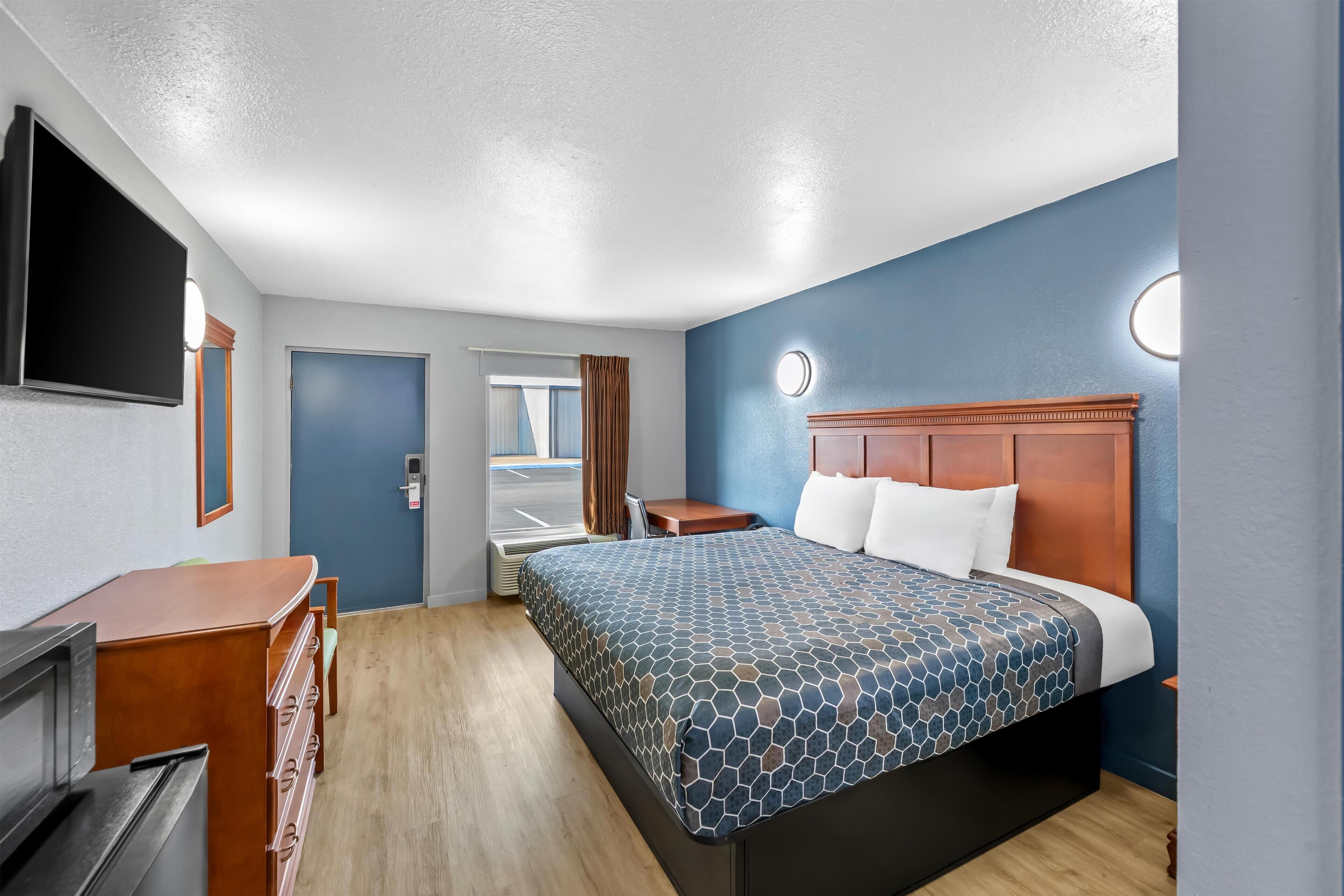 A hotel room with a bed, a desk, a TV, and a window with curtains.