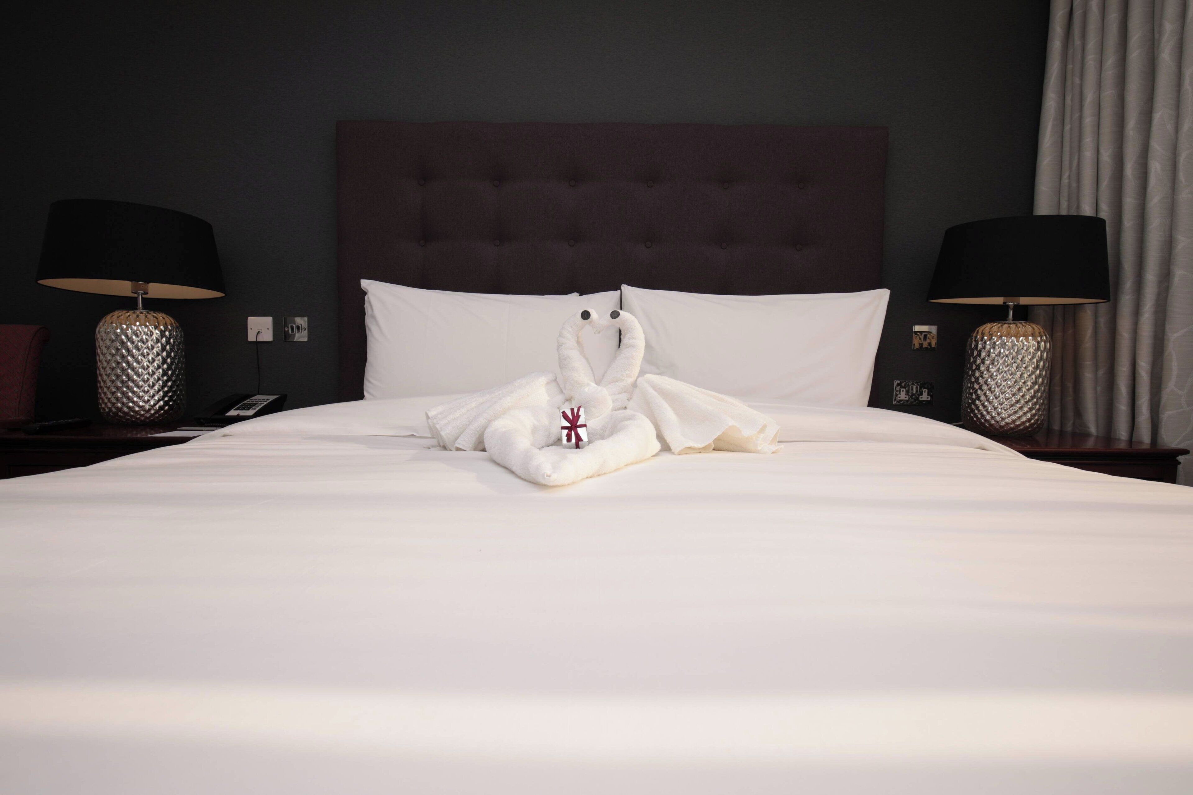 Habitación de hotel con una cama bien hecha, dos lámparas de noche y un cabecero oscuro.