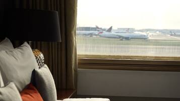 A hotel room with a bed, a lamp, and a view of airplanes on the tarmac through a window.