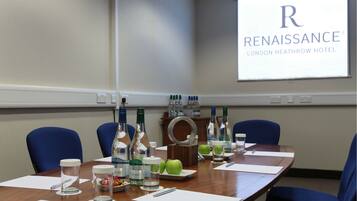 A conference room at the Renaissance London Heathrow Hotel with a long table, blue chairs, and various amenities like bottles, apples, and glasses.