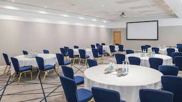 A conference room with round tables, blue chairs, and a projector screen.