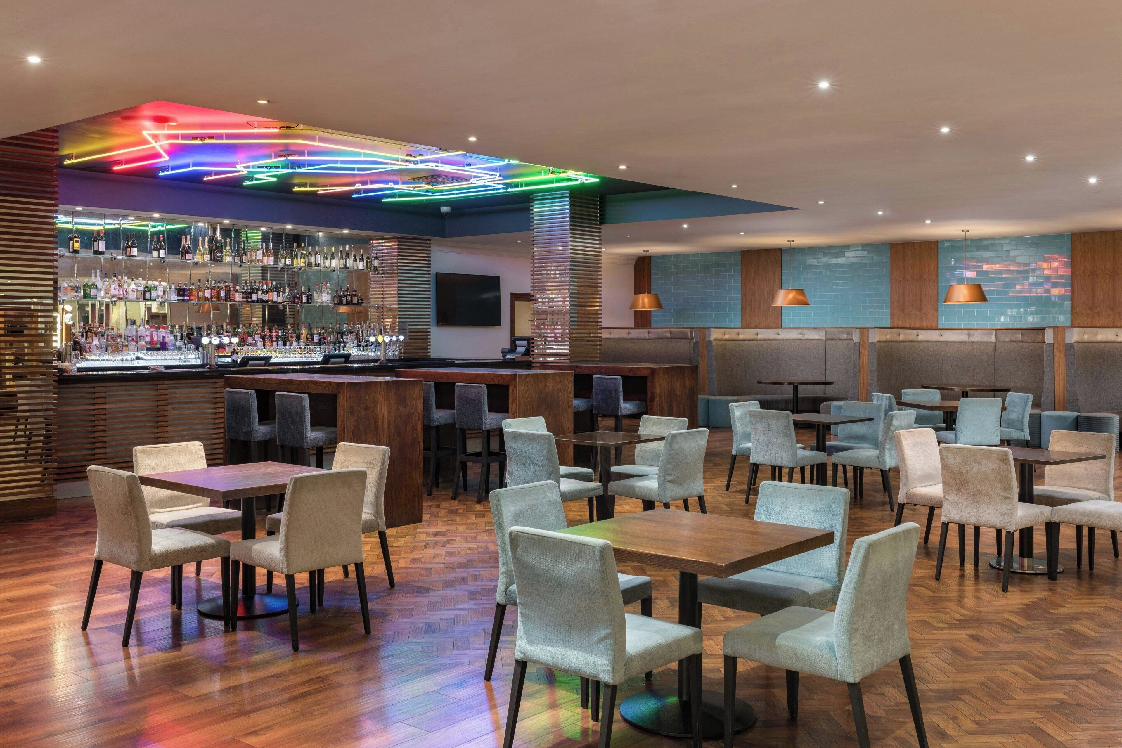 Un bar moderno con diversas opciones de asiento, incluyendo mesas y sillas, y una barra bien surtida.