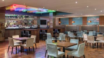 Un bar moderno con diversas opciones de asiento, incluyendo mesas y sillas, y una barra bien surtida.
