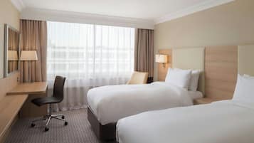 A hotel room with two beds, a desk, a chair, and a large window with curtains.