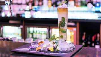 A bar setting with a tall glass of a beverage garnished with mint and ice, placed on a tray with decorative flowers and berries.