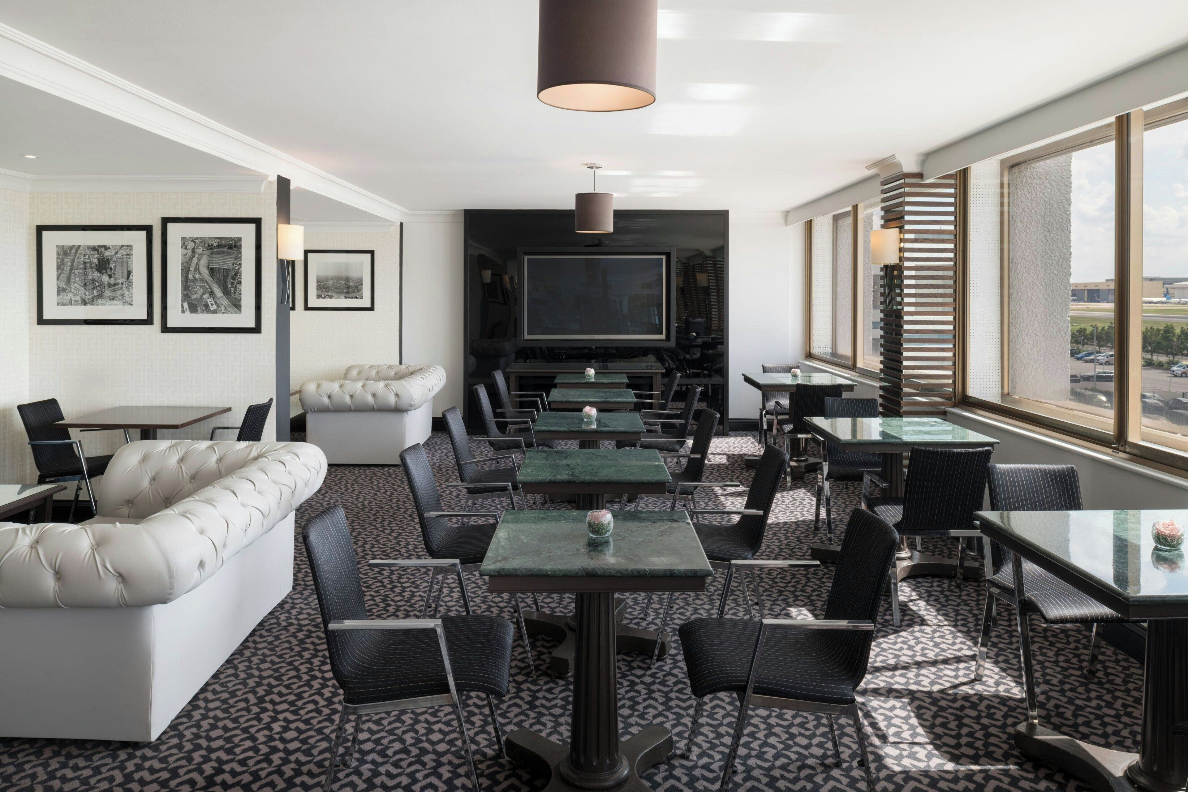 Ein stilvoller Lounge-Bereich mit einer Couch, Tischen, Stühlen und einem großen Bildschirm.