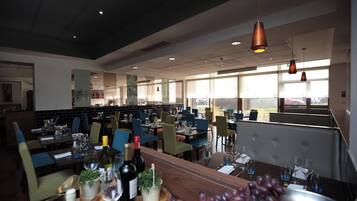 Un restaurante moderno con varias zonas de comedor, ventanas amplias y diversas opciones de asientos.