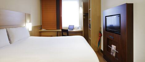 A hotel room with a large bed, a desk with a laptop, a television, and a wardrobe.