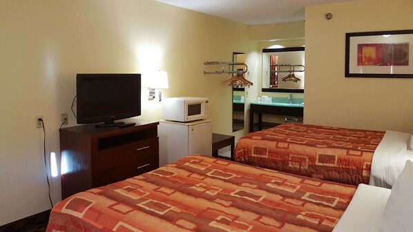 A hotel room with two beds, a television, a microwave, a small refrigerator, a desk, a mirror, and a framed picture on the wall. - Motel 6 Little Rock, AR - Airport (Little Rock)