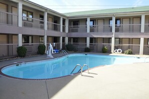 A pool area with a clear blue pool, a small white lounge chair, and a building with multiple balconies and windows. - Motel 6 Little Rock, AR - Airport (Little Rock)