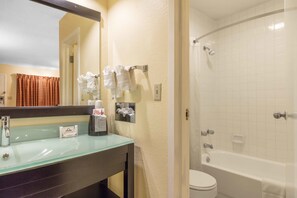 A bathroom with a glass sink, a mirror, a toilet, and a bathtub. - Motel 6 Little Rock, AR - Airport (Little Rock)