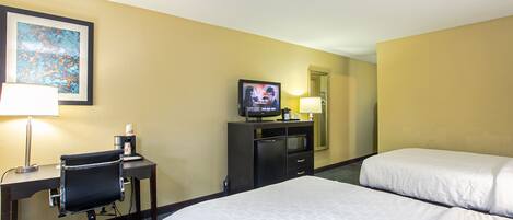 A hotel room with two beds, a desk with a chair, a television, and a lamp.