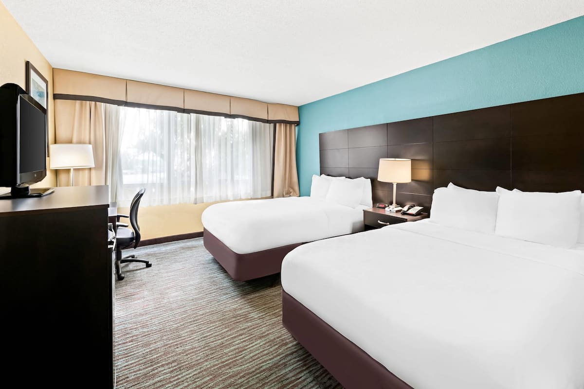A hotel room with two beds, a desk, a TV, and a window with curtains.