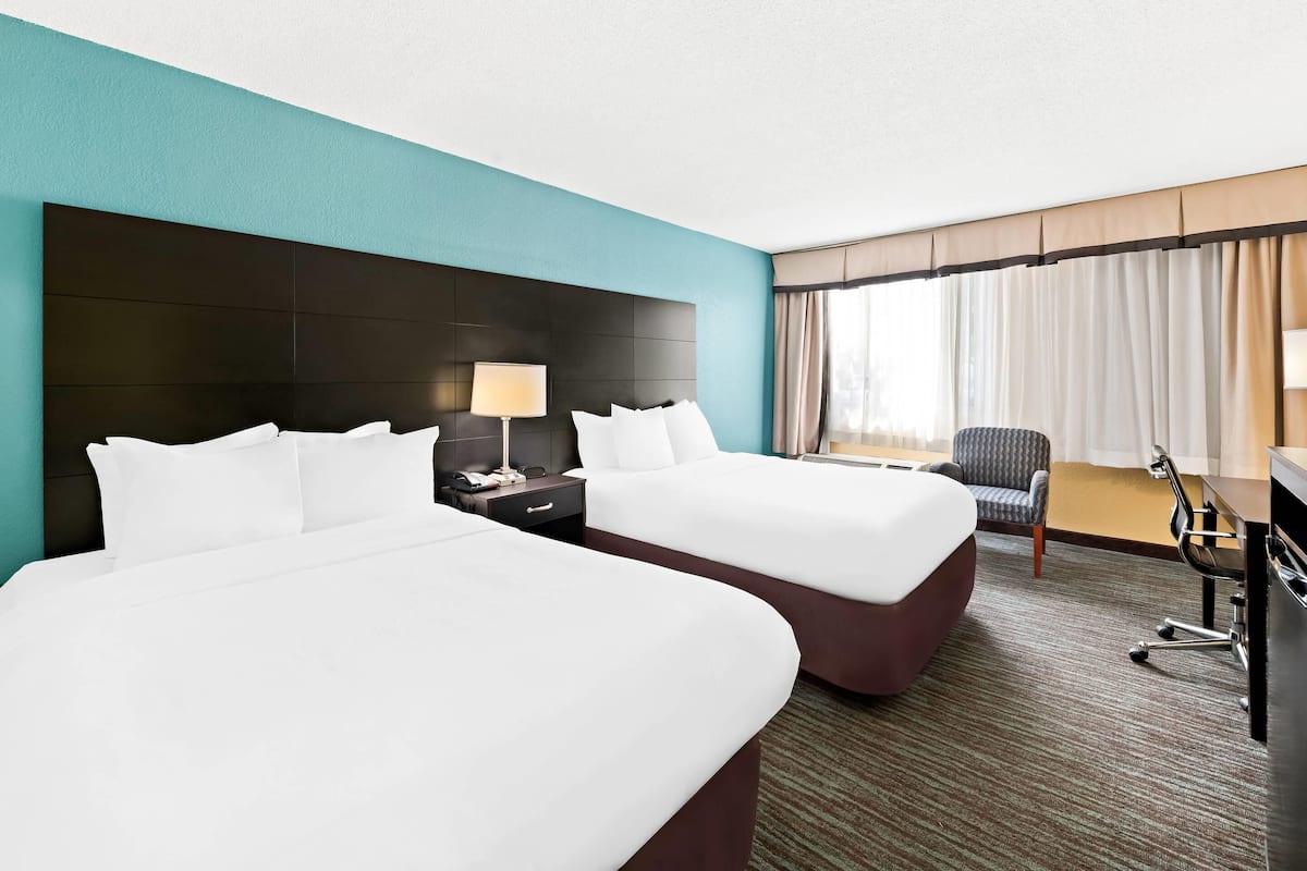 A hotel room with two beds, a desk, a chair, and a large window with curtains.