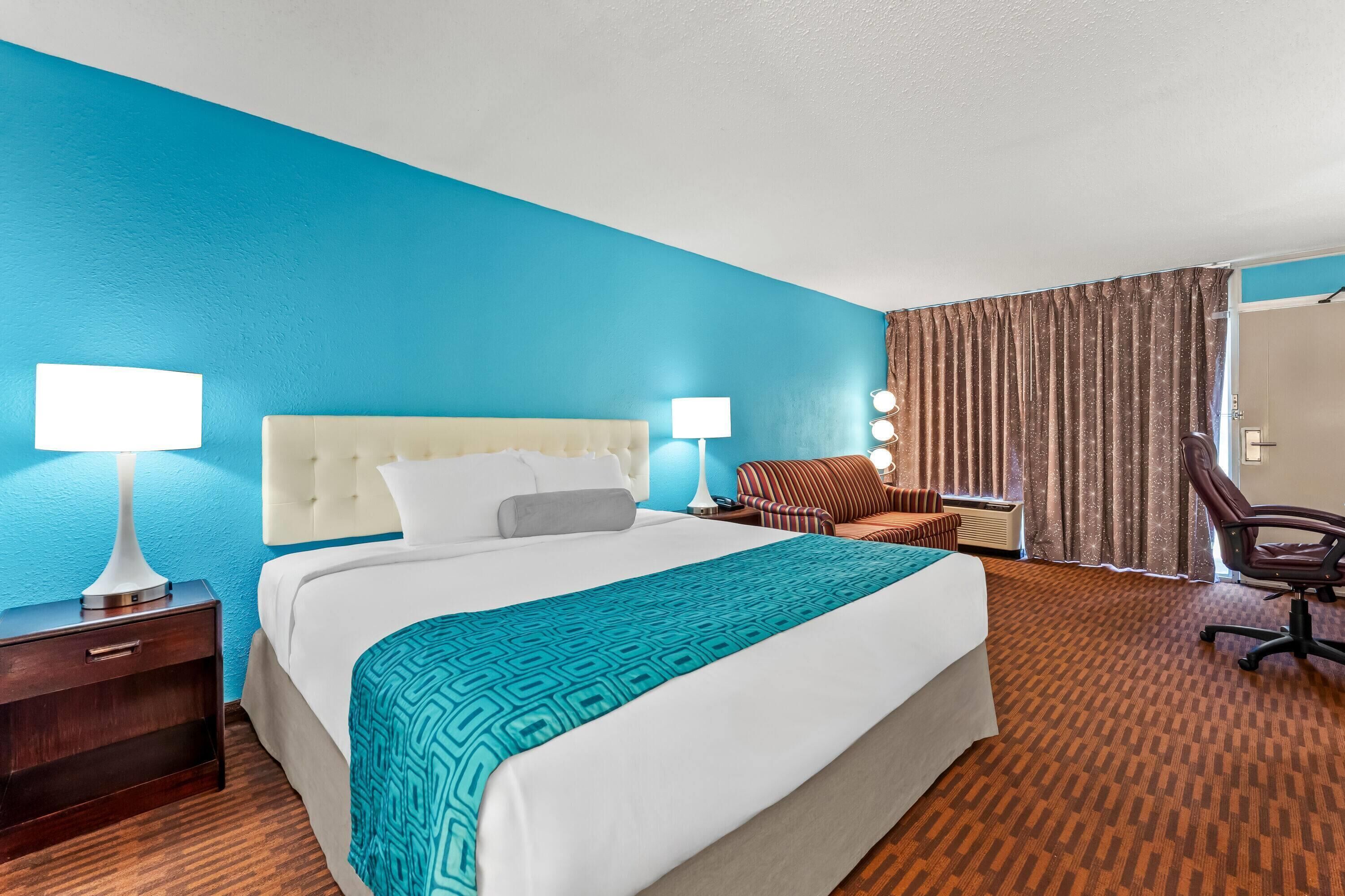 A hotel room with a large bed, two bedside tables with lamps, a sofa, a chair, and a curtain.
